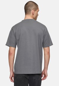 Grå bomulds T-shirt, korte ærmer, afslappet pasform. Rund hals design, glat tekstur, minimale syninger, båret med mørke jeans.