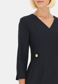 Granatowa sukienka z dekoltem w serek, rękawami o długości trzech ćwierć oraz złotymi guzikami przy talii. Gładki materiał z wyrafinowanym krojem.