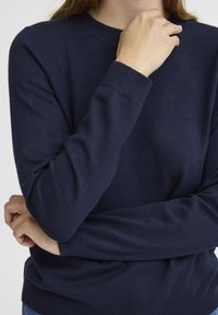 Pull bleu marine à col rond en tricot doux, avec des poignets et un ourlet côtelés, une texture lisse et une coupe ajustée.