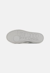 Hvit sneaker såle med teksturert overflate, med et fremtredende logo, sirkulære og diamantmønstre, og zigzag-mønster for grep.