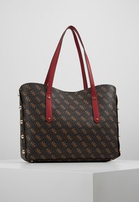 Tote bag met een zwarte, met patroon beklede buitenkant met bruine logo's, rode leren handvatten en gouden studs langs de zijkant. Glad oppervlak.