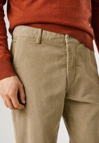 Beige corduroy broek met verticale ribbels en een sluiting met een knoop aan de voorkant, gecombineerd met een aansluitende roestkleurige trui.