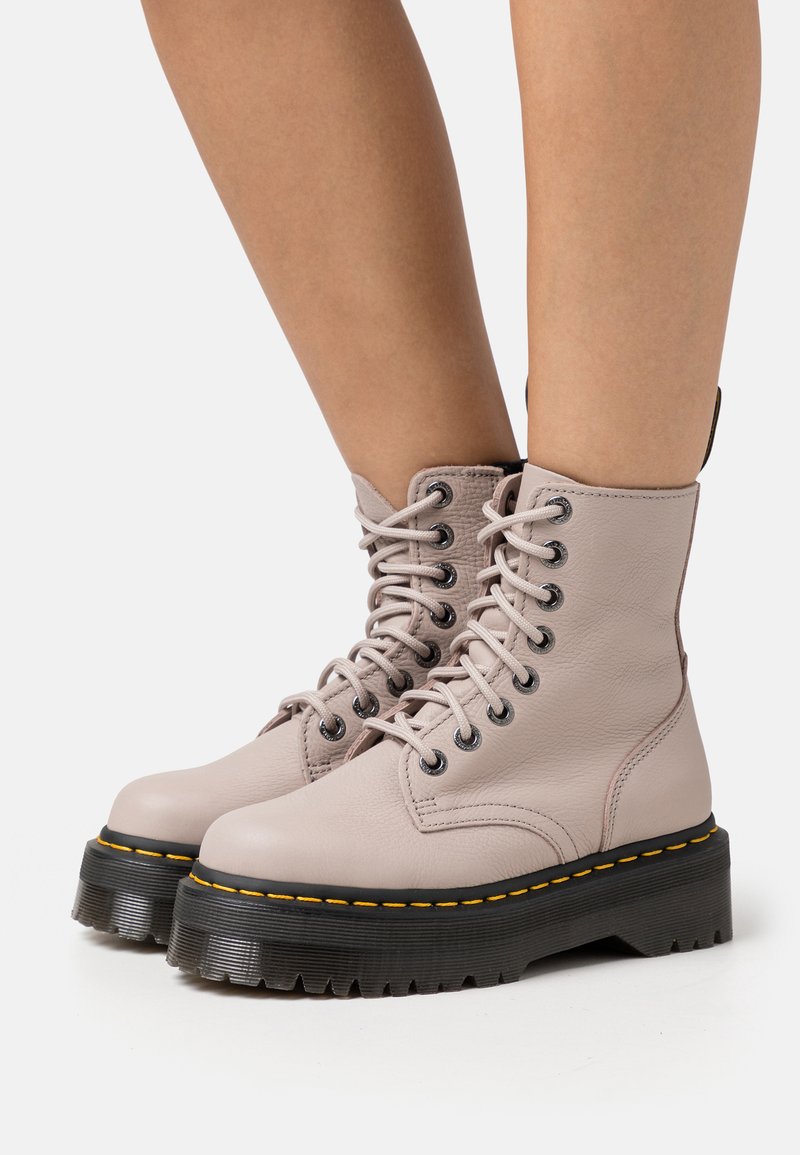 Botas de combate de cuero rosa claro con punta redonda, suelas de goma negra gruesa con un pespunte amarillo y detalles de cordones negros.
