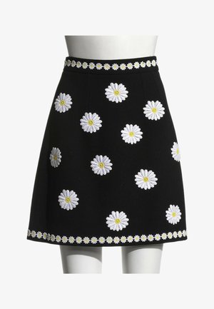 Jupe noire trapèze avec des marguerites blanches brodées aux centres jaunes, comportant une bordure de marguerites à la taille et à l'ourlet.