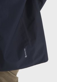 Marineblaues Gore-Tex-Jacke mit glatter Textur; verfügt über ein Logo am Saum. Das Design ist schlank und modern mit einer leichten Konstruktion.