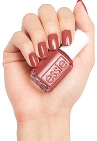 Essie nagellak in een medium rozenkleur, in een glazen fles met een witte dop, vastgehouden in een hand met manicured nagels van dezelfde tint.