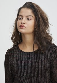 Top nero con strisce verticali di fili iridescenti, scollatura rotonda e spalle a palloncino. Tessuto morbido con una silhouette aderente.