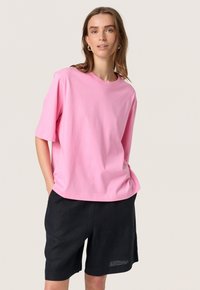 Rosa bomullströja med korta ärmar och rund halsringning, tillsammans med svarta shorts. Enkelt mönster, inga synliga mönster eller detaljer.