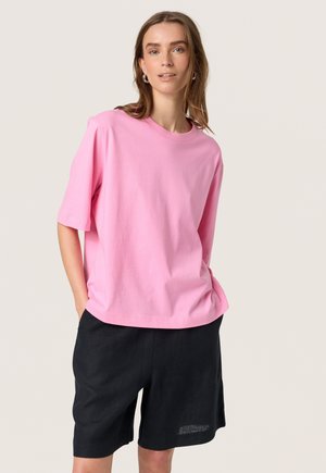 T-shirt en coton rose à manches courtes et col rond, associé à un short noir. Design simple, sans motifs ni accents visibles.