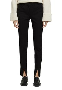 Svarta skräddarsydda byxor med smal passform, med framslitningar vid fållarna och en mjuk textur, tillsammans med svarta loafers.