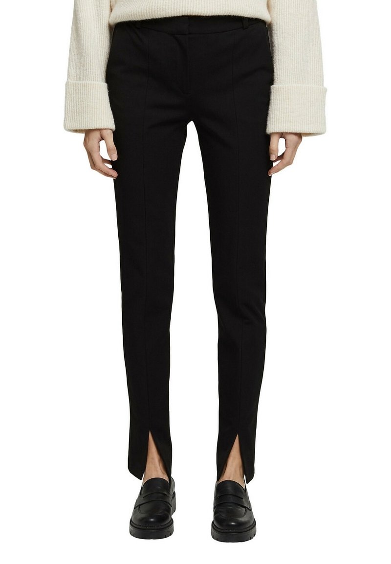 Svarta skräddarsydda byxor med smal passform, med framslitningar vid fållarna och en mjuk textur, tillsammans med svarta loafers.