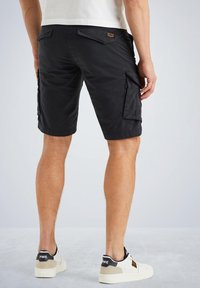Pantalones cortos cargo en algodón negro, con bolsillos laterales y un bolsillo de parche en la parte posterior. Combinados con zapatillas blancas con acentos negros.