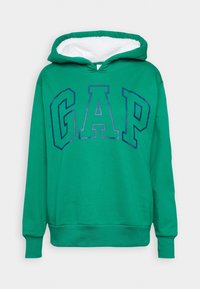 Sweat-shirt vert à capuche avec doublure en polaire blanche à l'intérieur de la capuche et "GAP" imprimé en grandes lettres bleues cerclées sur le devant.