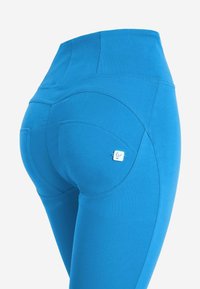 Leggings azzurri a vita alta realizzati in materiale elasticizzato, caratterizzati da cuciture curve e una piccola etichetta sulla tasca posteriore.