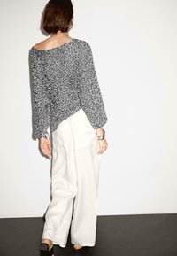 Black and white patterned loose-knit sweater with wide sleeves, paired with high-waisted white wide-leg pants and a silver cuff bracelet.