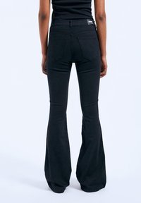 Black flared jeans with a high waist, made of denim. Features two back pockets, subtle stitching, and a flat waistband tag.