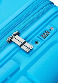 Valigia rigida blu con superficie texturizzata, doppie zip e una serratura a combinazione con tre quadranti. Elementi di design dettagliati visibili.