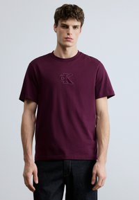 Burgundy short-sleeve t-shirt featuring an embroidered CK logo. Made from soft fabric with a classic crew neck design.