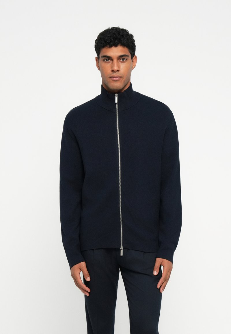 Sweater azul-marinho com fecho éclair, colarinho alto, feito de um material de malha suave, com um fecho prateado e um design de ajuste descontraído.