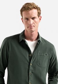 Groene button-up shirt van textuurstof, met een borstzak, witte binnenlaag en bruine knopen. Minimalistisch ontwerp.