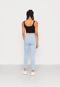 Top cropped preto com textura, combinado com jeans skinny de cintura alta azul claro e ténis brancos, visto pela parte de trás.