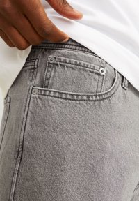Jeans in denim grigio con una vestibilità slim, dotati di una tasca frontale. Il tessuto presenta una sottile texture e dettagli di cucitura visibili.