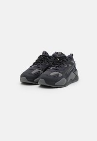 Un paio di sneakers sportive nere e grigio scuro con lacci e suole testurizzate su uno sfondo bianco.