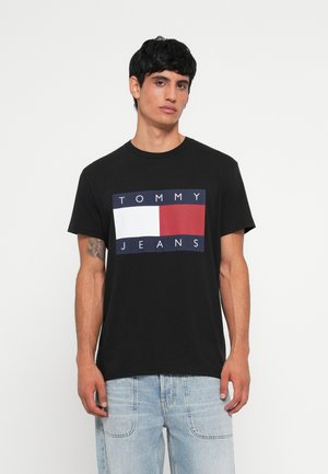 Sort bomulds t-shirt med et dristigt frontdesign med "TOMMY" i hvid og "JEANS" i hvid, sat mod en rød og hvid rektangulær baggrund.
