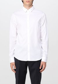 Camisa blanca de manga larga con cuello abotonado, hecha de una suave tela de algodón. Presenta un logo sutil en el pecho y una tapeta de botones estándar.