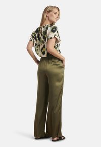 Korte mouwen, losse blouse met een groen, zwart en crème abstract patroon; gecombineerd met olijfgroene satijnen broek met wijde pijpen en zakken.