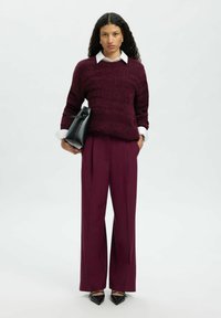 Bordo spalvos megztinis su tekstūruotomis juostelėmis, po juo baltas marškinių apykaklė; laisvo kirpimo, aukštu liemeniu slyvų spalvos kelnės; juoda rankinė ir smailiomis noselėmis batai.