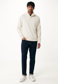 Suéter de mezcla de algodón crema con cuello alto y cierre a presión, combinado con jeans de mezclilla azul oscuro y zapatillas blancas. Diseño simple y casual.