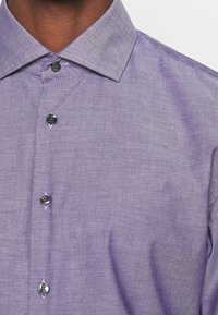 Levandulová košile na zapínání s texturovanou látkou, s špičatým límcem a šesti černými knoflíky na přední straně. Jednoduchý, moderní design.