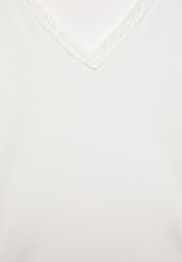 Fehér V-nyakú felső texturált csipkebetéttel a nyakkivágás mentén, sima anyagfelülettel és egyszerű, minimalista dizájnnal.