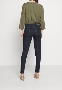 Mörkblå smala jeans med bakfickor, matchade med en olivgrön topp och remförsedda klackar med orm-mönster. Slät tyg, figursydd design.