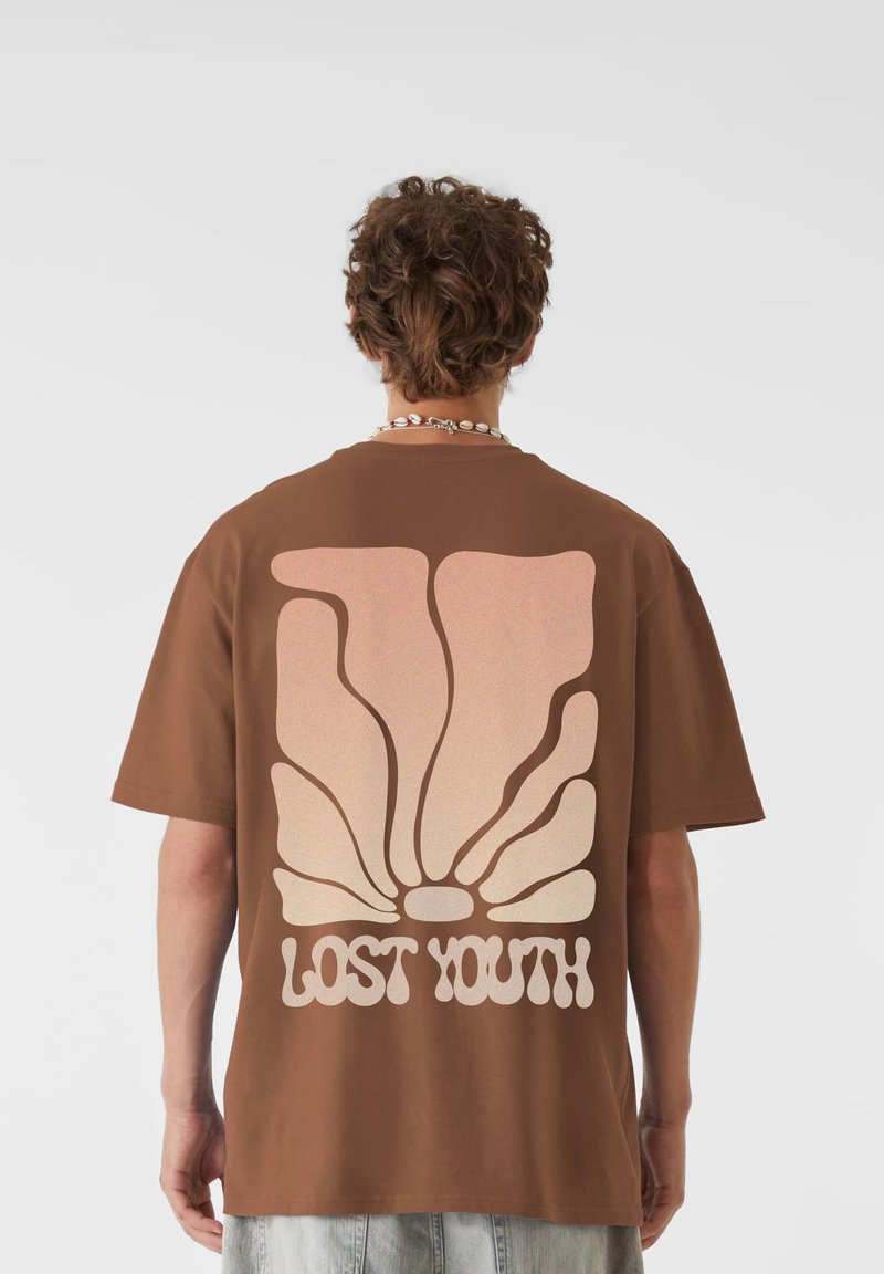 Barna, oversized t-shirt, amelynek hátulját egy nagy, pasztell színű, átmenetes kagyló grafika díszíti, alatta pedig a "LOST YOUTH" felirat található, vastag betűtípussal.