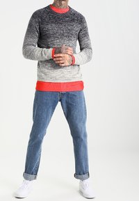 Stickad tröja med en övergång från mörkgrått till ljust grått, med en ljusröd krage och muddar, tillsammans med blåjeans och vita sneakers.