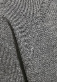 Tessuto a maglia grigio che mette in risalto una trama a coste con una leggera lucentezza. Il primo piano evidenzia i dettagli delle cuciture e la superficie morbida del tessuto.