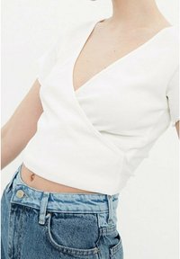 Top bianco avvolgente con maniche corte, tessuto testurizzato e scollatura a V, abbinato a jeans in denim azzurro chiaro a vita alta.