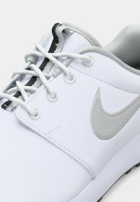 White sneaker made of synthetic leather, featuring gray accents, rounded toe, flat laces, and a textured Nike logo on the side.