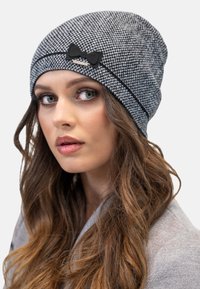 Beanie grigio intrecciato con un motivo a quadri testurizzato, accentuato da un fiocco in feltro nero e da una sottile striscia nera. Tessuto morbido e stretchabile.