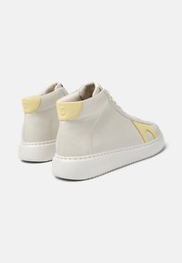 High-top sneakers in light beige leather with a yellow heel accent, white rubber sole, and textured surface detail.