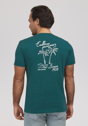 Mężczyzna o ciemnych włosach noszący morsko-zieloną koszulkę z białą grafiką palmy i napisem „Endless summer Since 1908 Lee Cooper” na plecach.