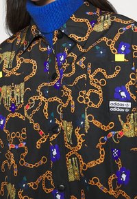 Svart skjorta med färgglada kedjemönster, leoparder och blommor. Har en bröstficka och ett "adidas"-logomärke. Blå polokrage under.