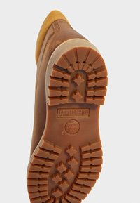 Timberland-støvlet sål med et robust brunt gummidesign, dybe slidbaner og Timberland-logoet præget nær hælen.