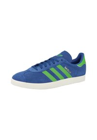 Sneaker blu scamosciato con tre strisce verdi e una suola in gomma bianca. La parola "GAZELLE" è visibile sul lato.