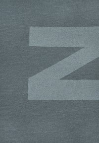 Textil in gedämpftem Blau mit einem größeren hellblauen geometrischen Muster. Der Stoff hat eine strukturierte Strickoberfläche. Fokus auf Kontrast und Designelemente.