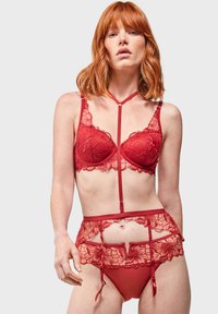 Rode kanten lingerieset bestaande uit een beha met gevoerde cups en bloemmotieven, gecombineerd met een transparante kanten guêpière en bijpassende slip.