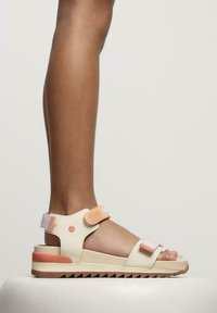 Sandalias crema y melocotón con correas de Velcro ajustables y una suela gruesa con borde aserrado. Superficie suave, diseño minimalista.