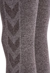 Grijze leggings van textuurstof, met een donker chevronpatroon langs de zijkant. Close-up focus op materiaal- en ontwerpdetaillering.